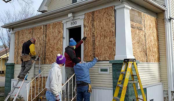 A group of people work to repair broken and boarded up windows